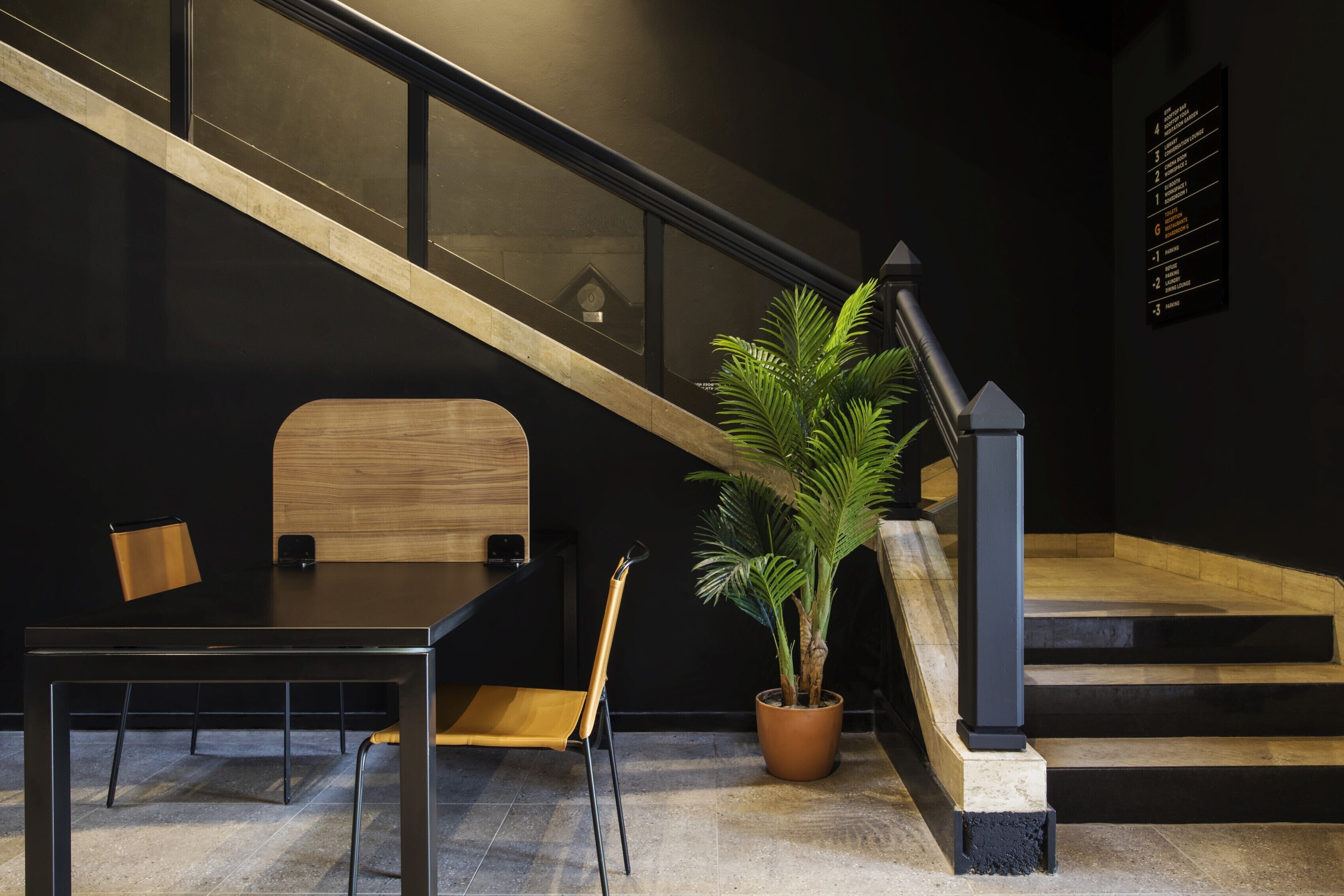 Un interior moderno con una escalera, un banco de madera, una mesa, sillas y una planta en maceta.