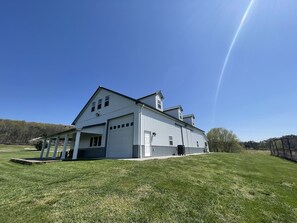 A large white building with multiple garage doors and a covered porch area. - The Barndominium at Berkeley Ridge - Book your getaway today! (BERKELEY SPRINGS)