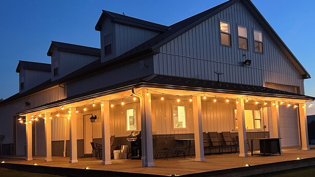 A two-story house with a covered patio area, string lights, and outdoor seating. - The Barndominium at Berkeley Ridge - Book your getaway today! (BERKELEY SPRINGS)