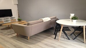 A modern living room with a grey sofa, a round dining table with black chairs, a small white table, and a TV on a white stand. - GET ★ QUIET ★ WIFI TERRACE (Revel)