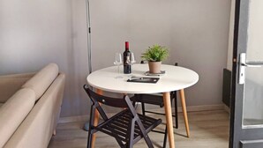 A small, round dining table with a potted plant, two wine glasses, and a bottle of wine. A beige sofa and a floor lamp are in the background. - GET ★ QUIET ★ WIFI TERRACE (Revel)