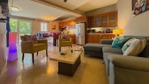 Een ruime woonkamer met een bank, stoelen, een salontafel en een keuken op de achtergrond.
