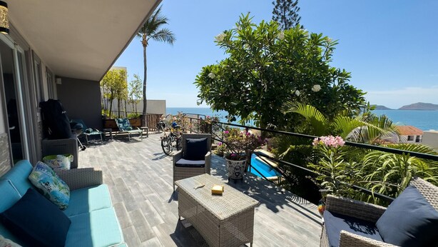 Een balkon met rieten meubilair, een zwembad en uitzicht op zee.