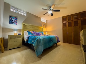 Un dormitorio con cama, mesitas de noche, ventilador de techo y armario.