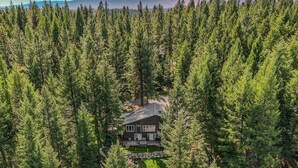 A cabin surrounded by dense forest, a clear path leading to the cabin, and a dock with a boat. - Pines on the Pond - Large home on Rio Vista Pond with dock, hot tub, amazing views (McCall)