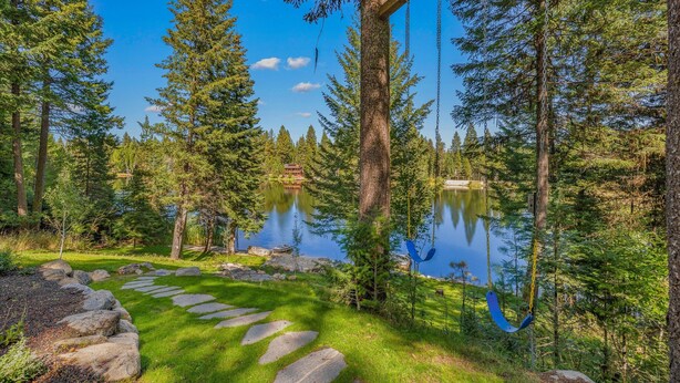 A serene forest with a clear lake, a stone pathway, and a swing. - Pines on the Pond - Large home on Rio Vista Pond with dock, hot tub, amazing views (McCall)
