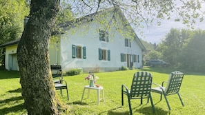 A white house with green shutters, a lawn, and two chairs.