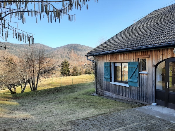 A wooden house with a tiled roof, a small window with shutters, and a paved driveway.