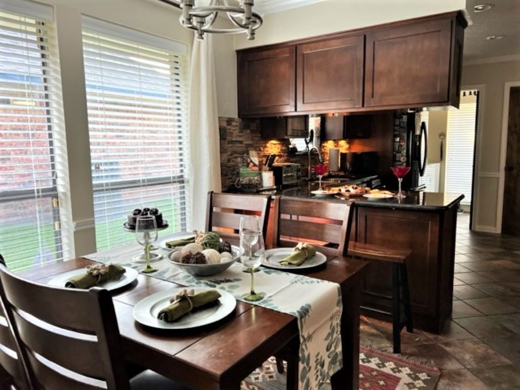 A dining area with a table set for four, wooden chairs, and a view through the window.
