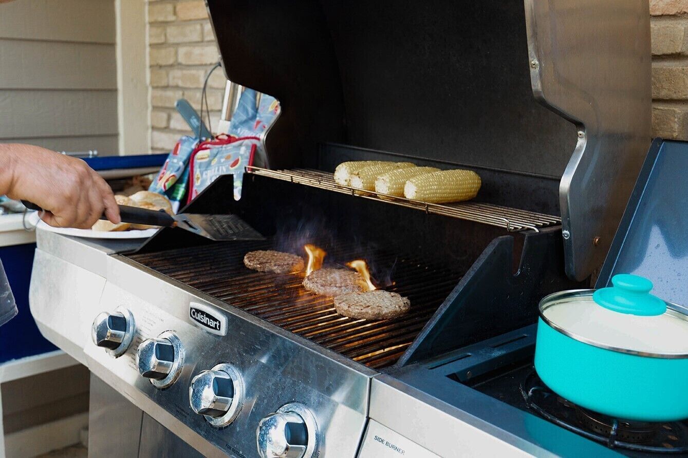 A Cuisinart grill with hamburgers and corn on the cob being cooked.