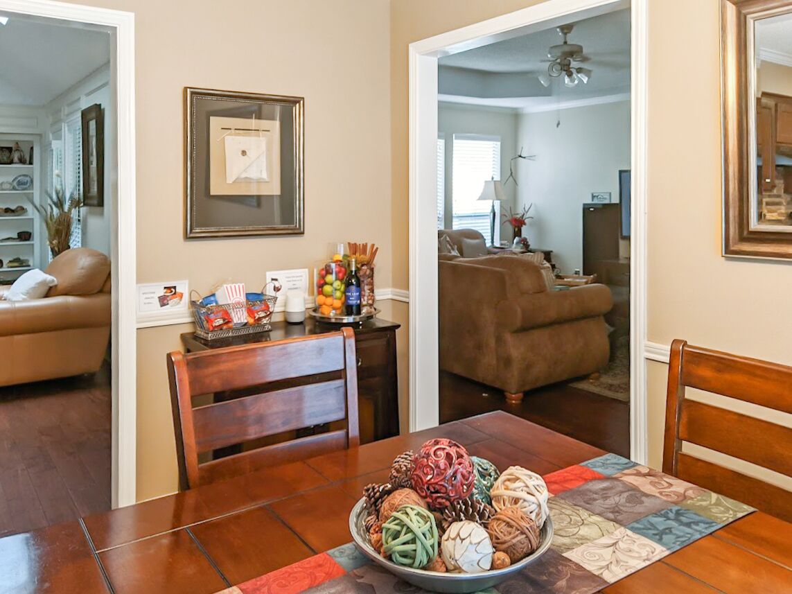 A dining area with a table set for four, a bowl of decorative items, and a framed picture on the wall.