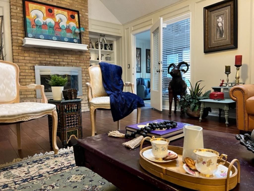 A cozy living room with a fireplace, a dog statue, and a dining table set with tea cups and a book.