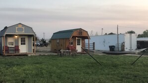 Two small wooden sheds with attached porches, a grassy field, and a white trailer in the background. - Cute Farmhouse Cottage  (Oakley)
