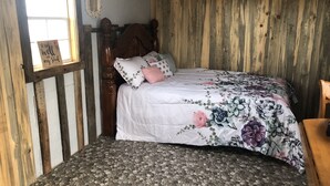 A bedroom with a bed, wooden walls, a window, and a mirror. - Cute Farmhouse Cottage  (Oakley)