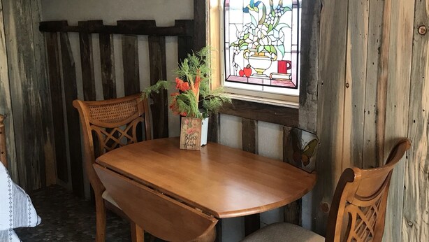 A wooden dining table with chairs, a vase with flowers, and a stained glass window with a floral design. - Cute Farmhouse Cottage  (Oakley)