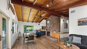 A spacious living area with a wooden ceiling, a brick fireplace, and a dining area with a table and chairs.