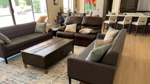 A modern living room with a sectional sofa, a coffee table, and a dining area with bar stools. - Gorgeous Contemporary Palm Desert Home.  Ask about March - April discount!! (Palm Desert)