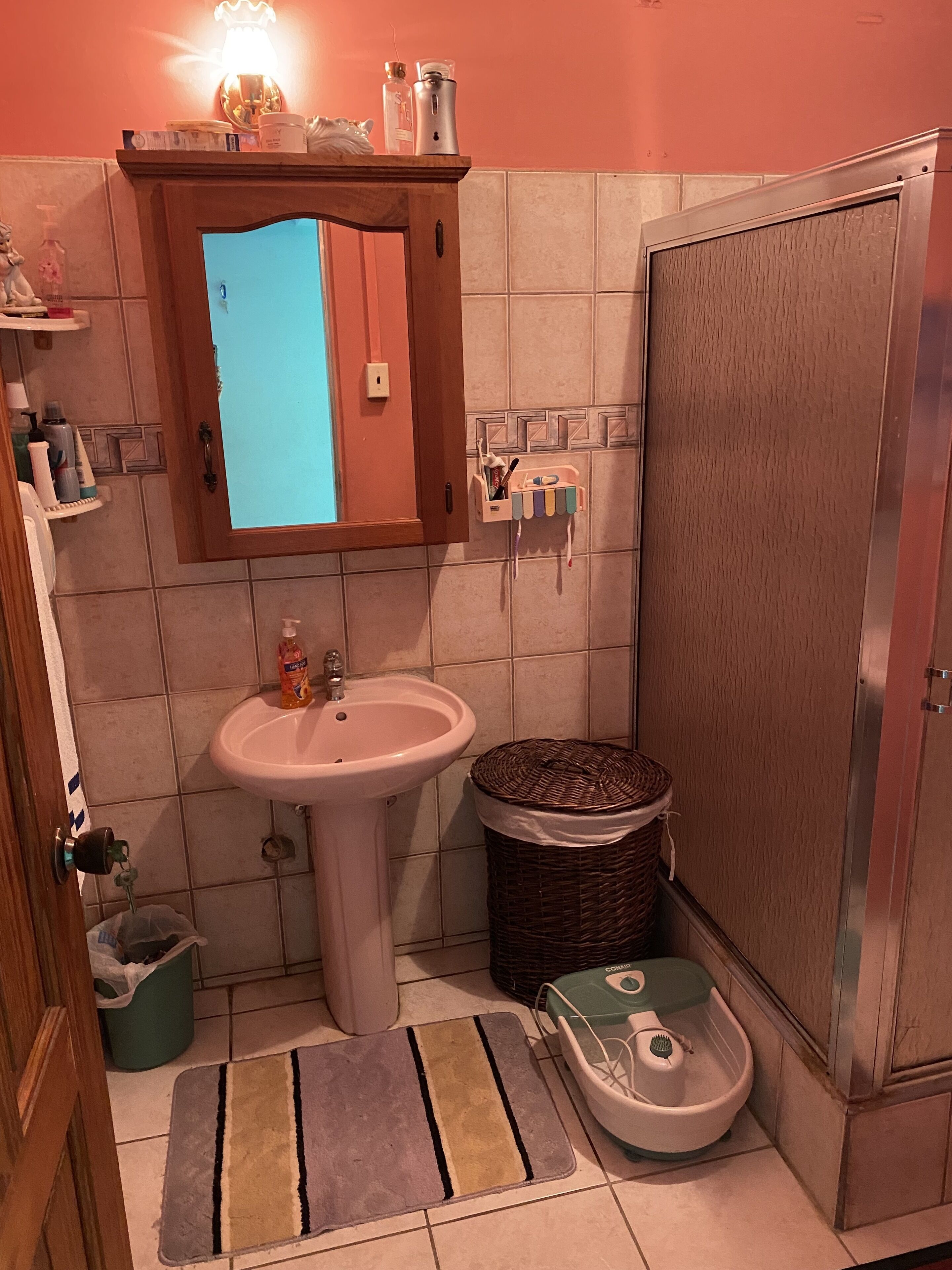 A bathroom with a sink, a mirror, a shower, and a small shelf with toiletries.