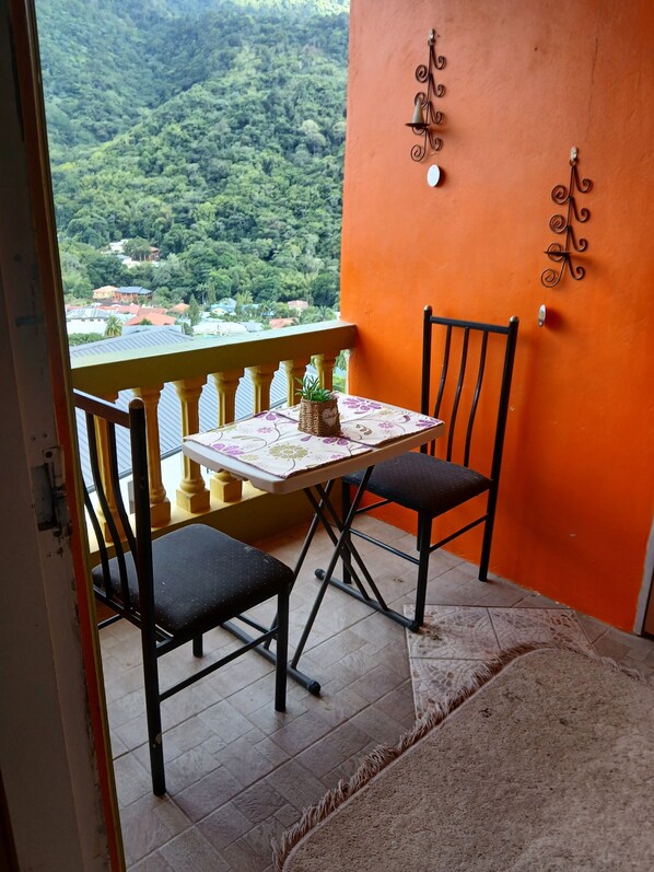 A balcony with a table, two chairs, and a view of a forested area. - QBR Balcony Suite (St. Joseph)