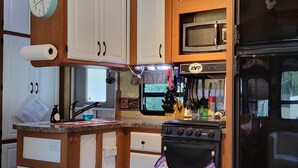 A compact kitchen with wooden cabinets, a microwave, a stove, and a refrigerator.