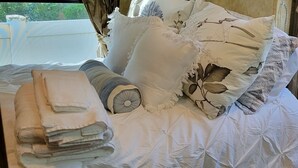 A neatly made bed with white linens and decorative pillows, a rolled towel, and a small round pillow.