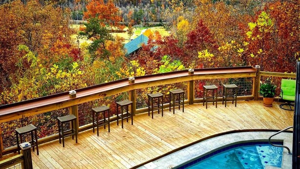 A wooden deck with outdoor seating overlooking a pool and a scenic view of autumn foliage and mountains.