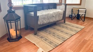 A room with a wooden floor, a bench with a fluffy white cover, a patterned rug, a black lantern with candles, and a window with a view of trees. - Peaceful Ranch-style Single level 3B Retreat (Hillsboro)