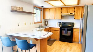 A kitchen with wooden cabinets, a black stove, a refrigerator, and two blue bar stools. - Peaceful Ranch-style Single level 3B Retreat (Hillsboro)
