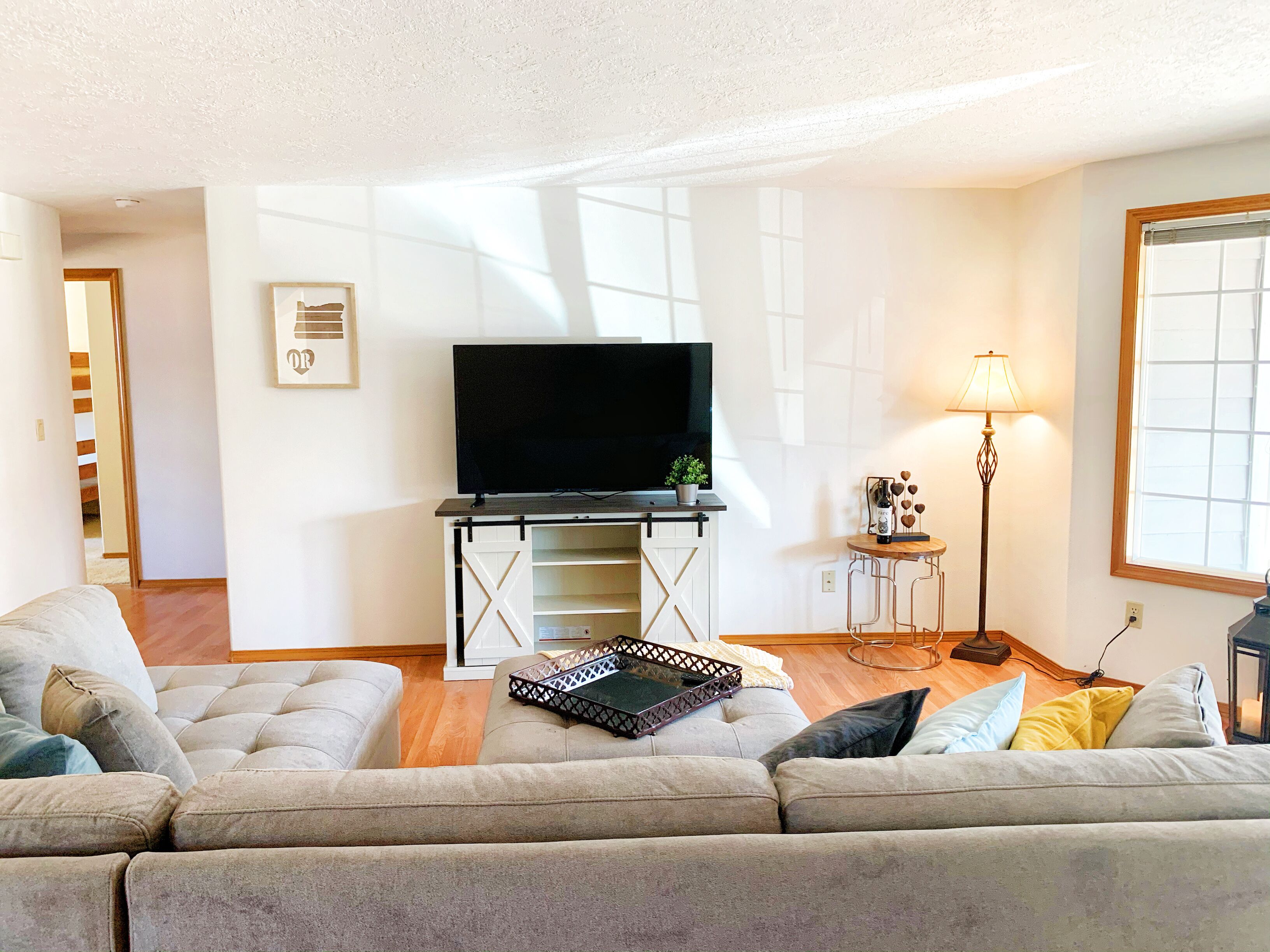 A living room with a sofa set, a TV on a stand, a lamp, and a window.