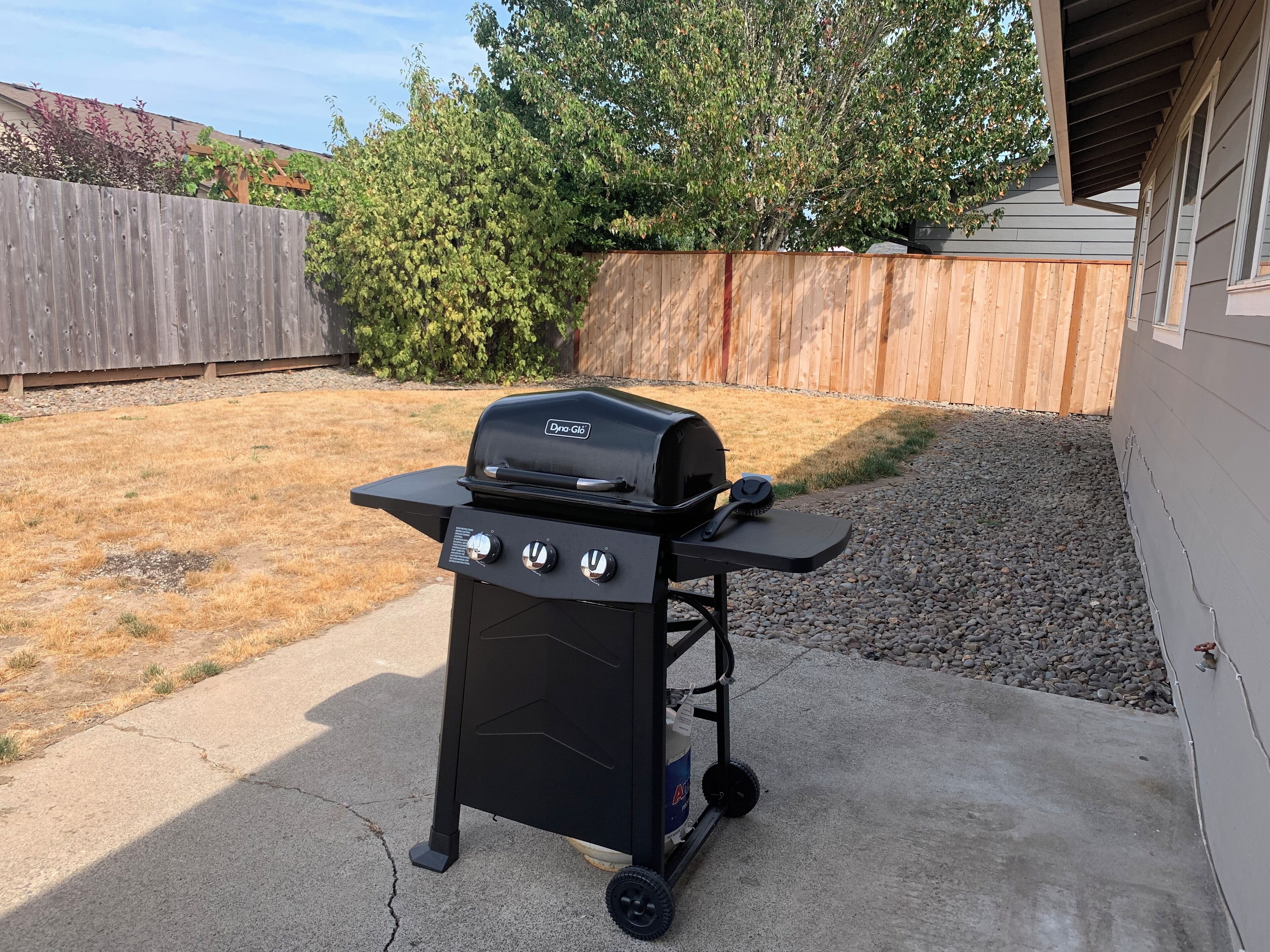 Una parrilla portátil con pantalla digital, un cepillo para limpieza y un depósito de combustible.