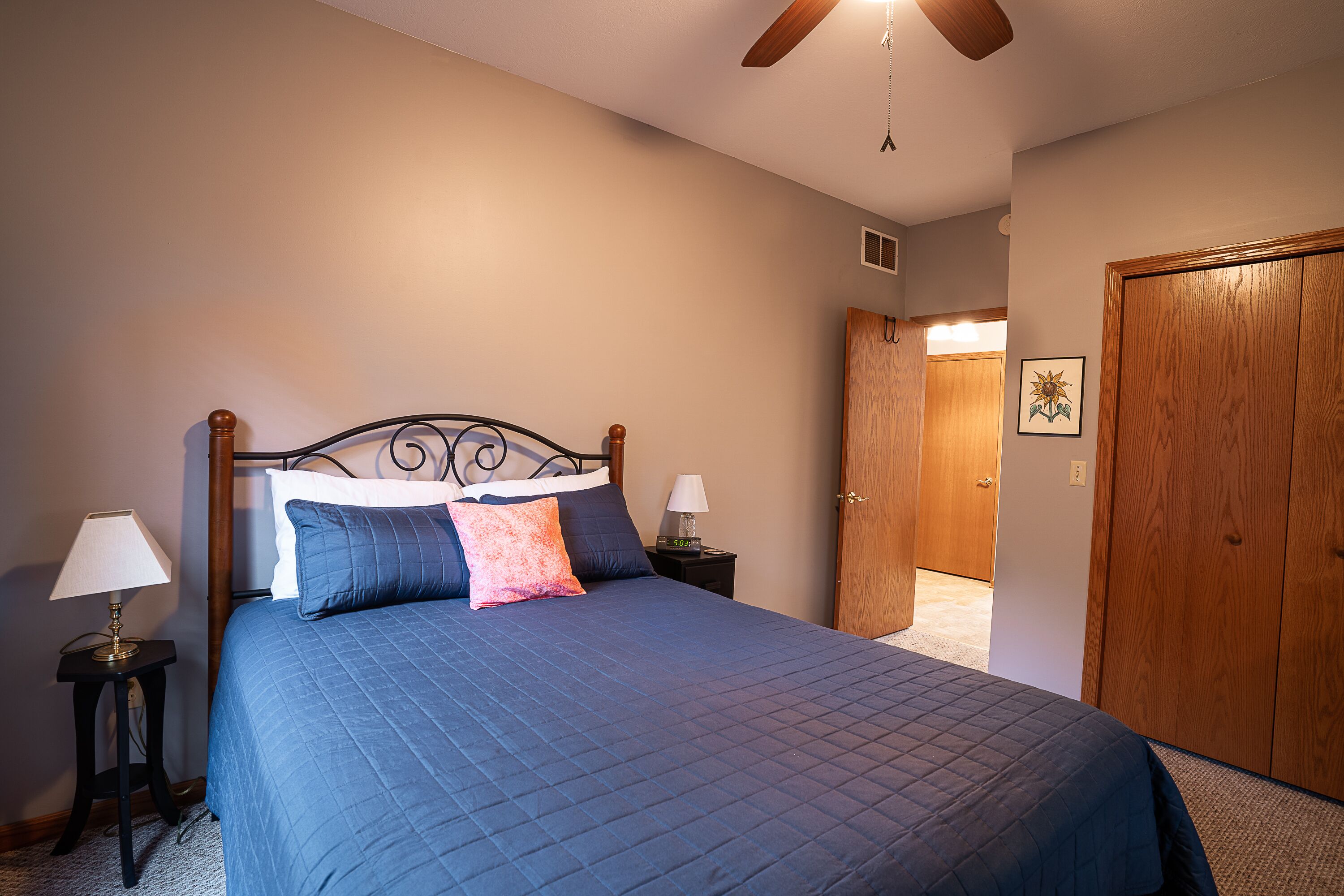 A bedroom with a bed, two bedside tables with lamps, a wooden door, and a ceiling fan.