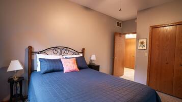 A bedroom with a bed, two bedside tables with lamps, a wooden door, and a ceiling fan.