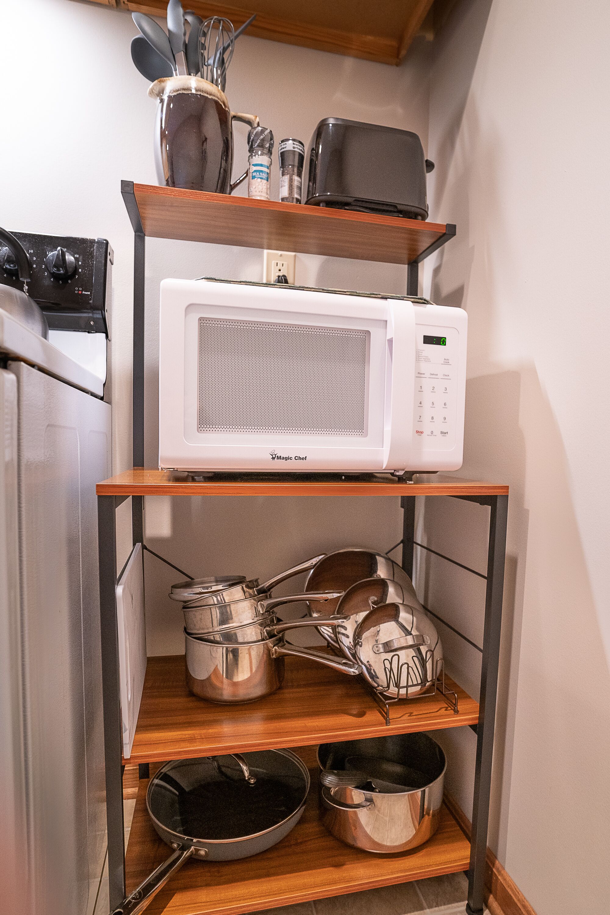 Una cocina con un microondas en un estante, una estufa y diferentes ollas y sartenes.
