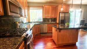 Eine moderne Küche mit Granit-Arbeitsplatten, Holzschränken, einem Edelstahl-Kühlschrank und einem eingebauten Geschirrspüler.