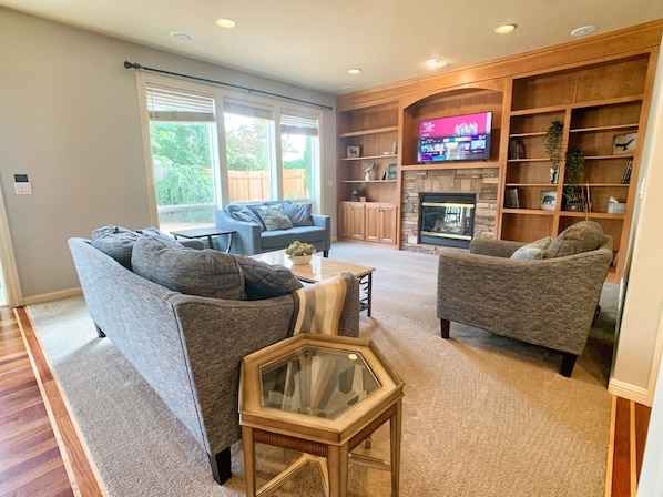 Ein Wohnzimmer mit zwei grauen Sofas, einem Couchtisch mit Glasplatte und einem Kamin aus Stein.
