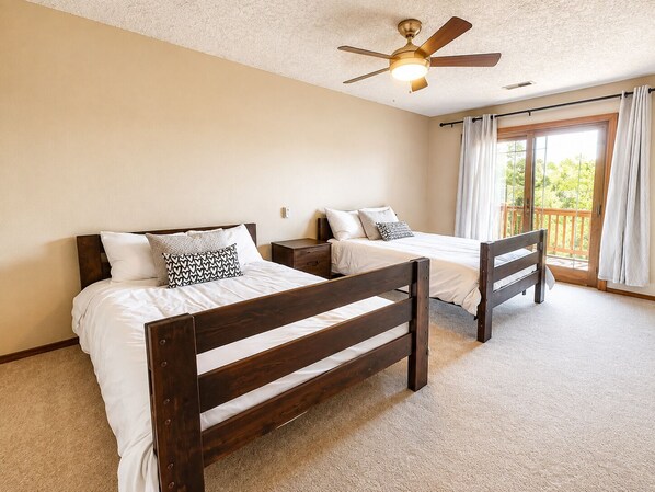 Een slaapkamer met twee houten bedden, een plafondventilator en een balkon met gordijnen.