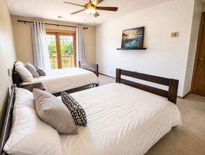 A bedroom with two beds, a ceiling fan, a window with curtains, and a painting on the wall.