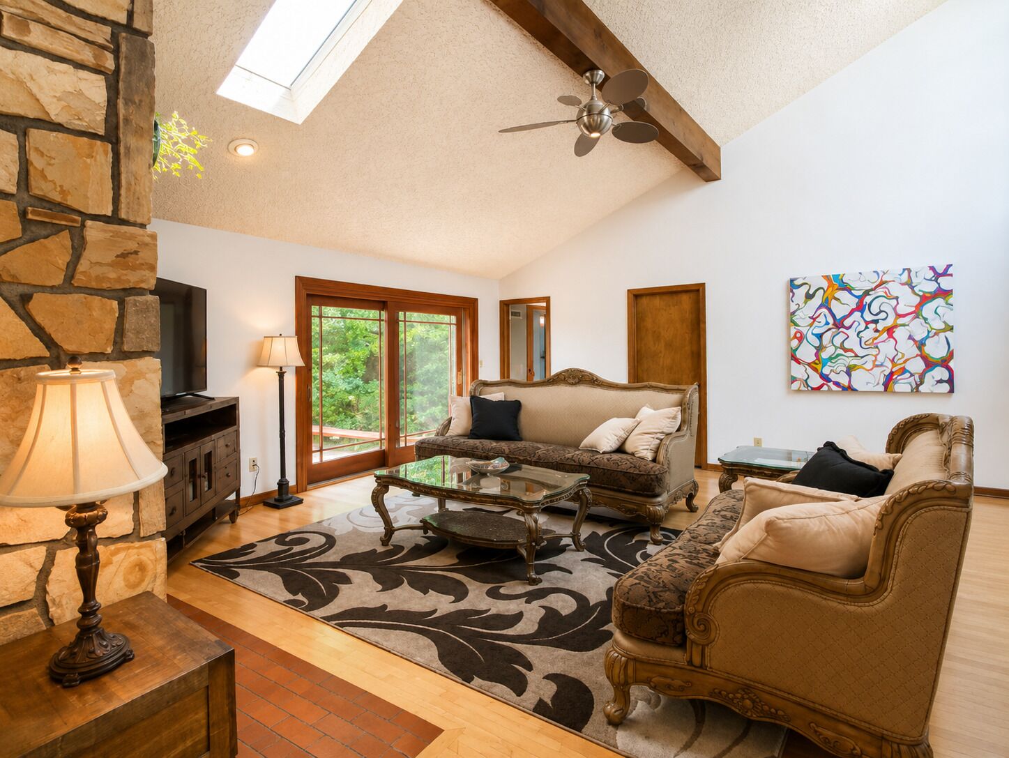 A spacious living room with a stone wall, a ceiling fan, a fireplace, and a large window.