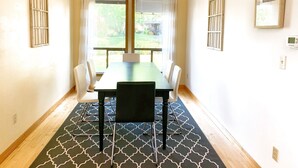 Un espace repas comprenant une table et des chaises, un tapis à motifs et une vue sur la verdure à l’extérieur.