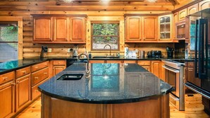 A spacious kitchen with wooden cabinets, a large island with a sink, and a view of the outdoors through a window. - Massive 7BR Cabin Sleeps 18! (Sevierville)