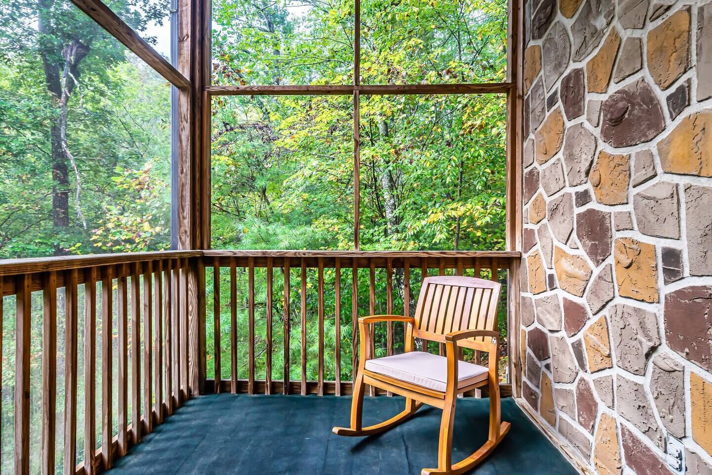 Une chaise berçante en bois sur un balcon, avec un mur en pierre et une vue sur une forêt.