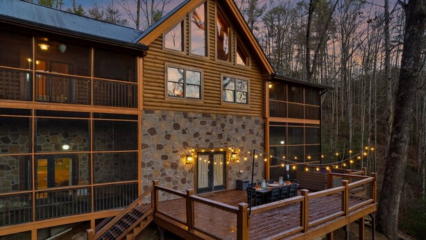 A log cabin with a stone facade, large windows, and a deck with outdoor seating. - Massive 7BR Cabin Sleeps 18! (Sevierville)