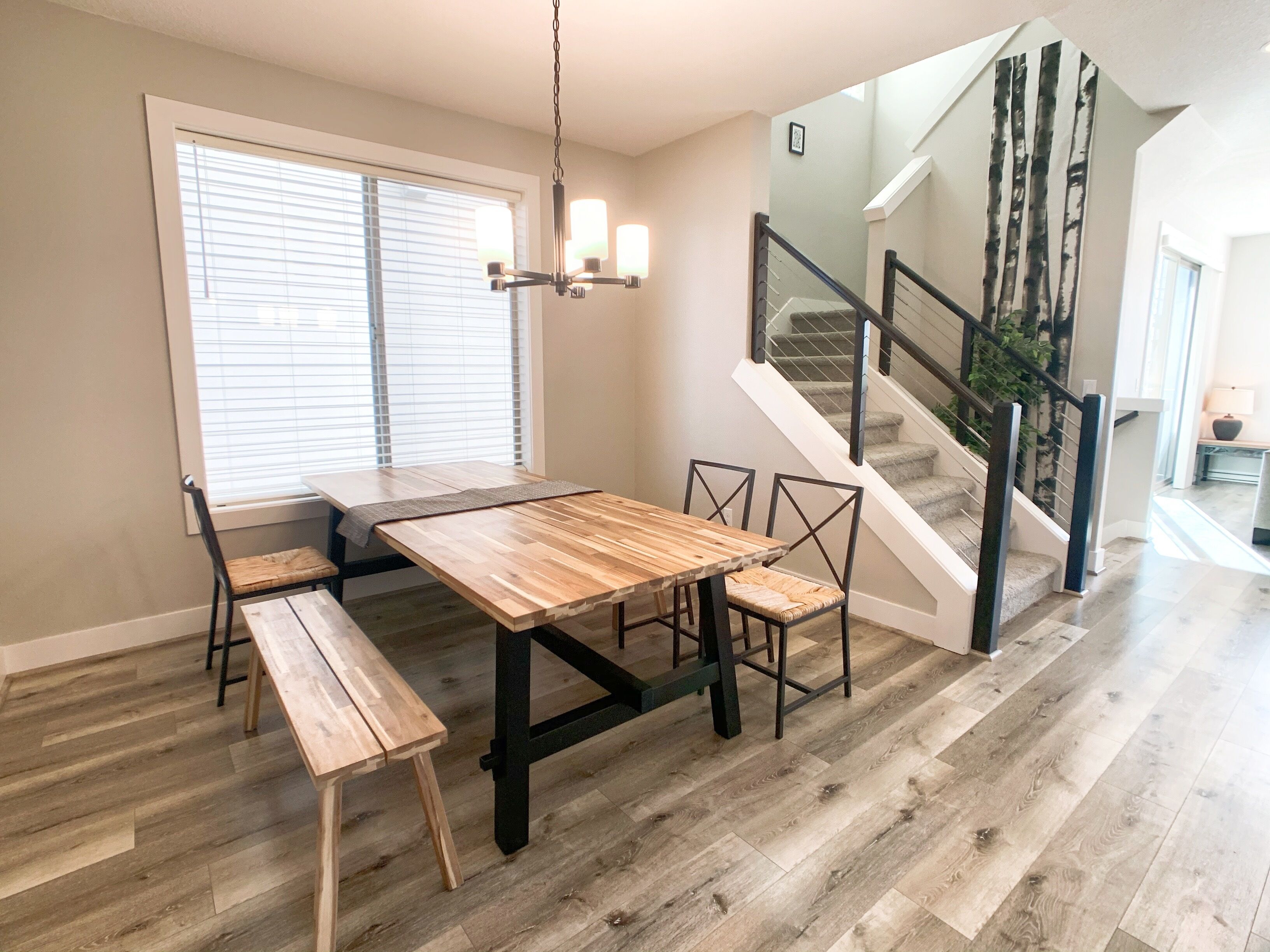 A dining area with a wooden table and chairs, a bench, and a chandelier.