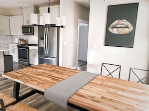 A modern kitchen with stainless steel appliances, a wooden dining table, and a patterned bench.