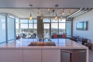 A modern kitchen with a large island, a dining area with chairs, and a view of the city. - Modern Downtown SD Apartment Stunning City Views (San Diego)