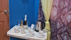 Een kleine tafel met een witte tafelkleed, een Daewoo elektrische waterkoker, een fles Moscato wijn en diverse witte kopjes en schoteltjes.