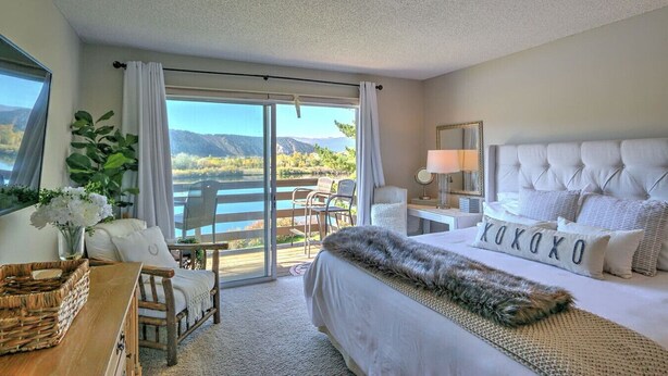 A bedroom with a large bed, a desk, a chair, and a view of a lake and mountains through a sliding glass door. - Condo on pond w/2 Fishing Badges, 24 Mi. to Aspen! (Carbondale)