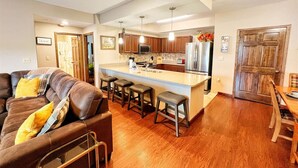 A modern kitchen with wooden cabinets, a central island with stools, and a dining area with a wooden table and chairs. - HV 102, great view, Handicapped accessible (Gatlinburg)