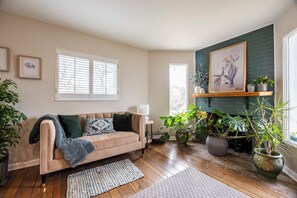 En hyggelig stue med en beige sofa, en pejs og flere krukkeplanter.