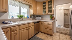 A kitchen with wooden cabinets, a microwave, a sink, and a window with lace curtains.